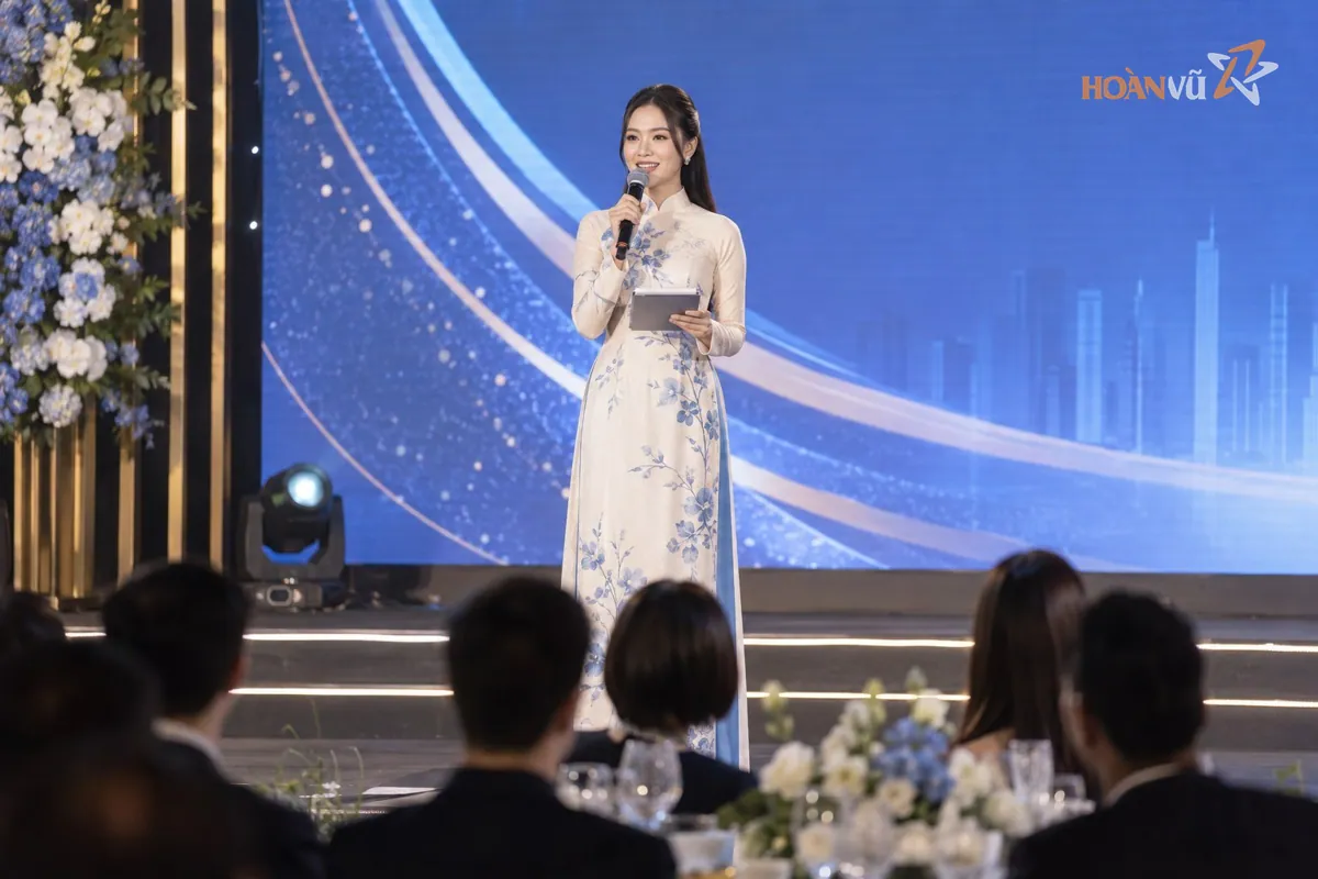 Nữ MC mặc áo dài dẫn chương trình lễ kỷ niệm doanh nghiệp, cầm micro và kịch bản