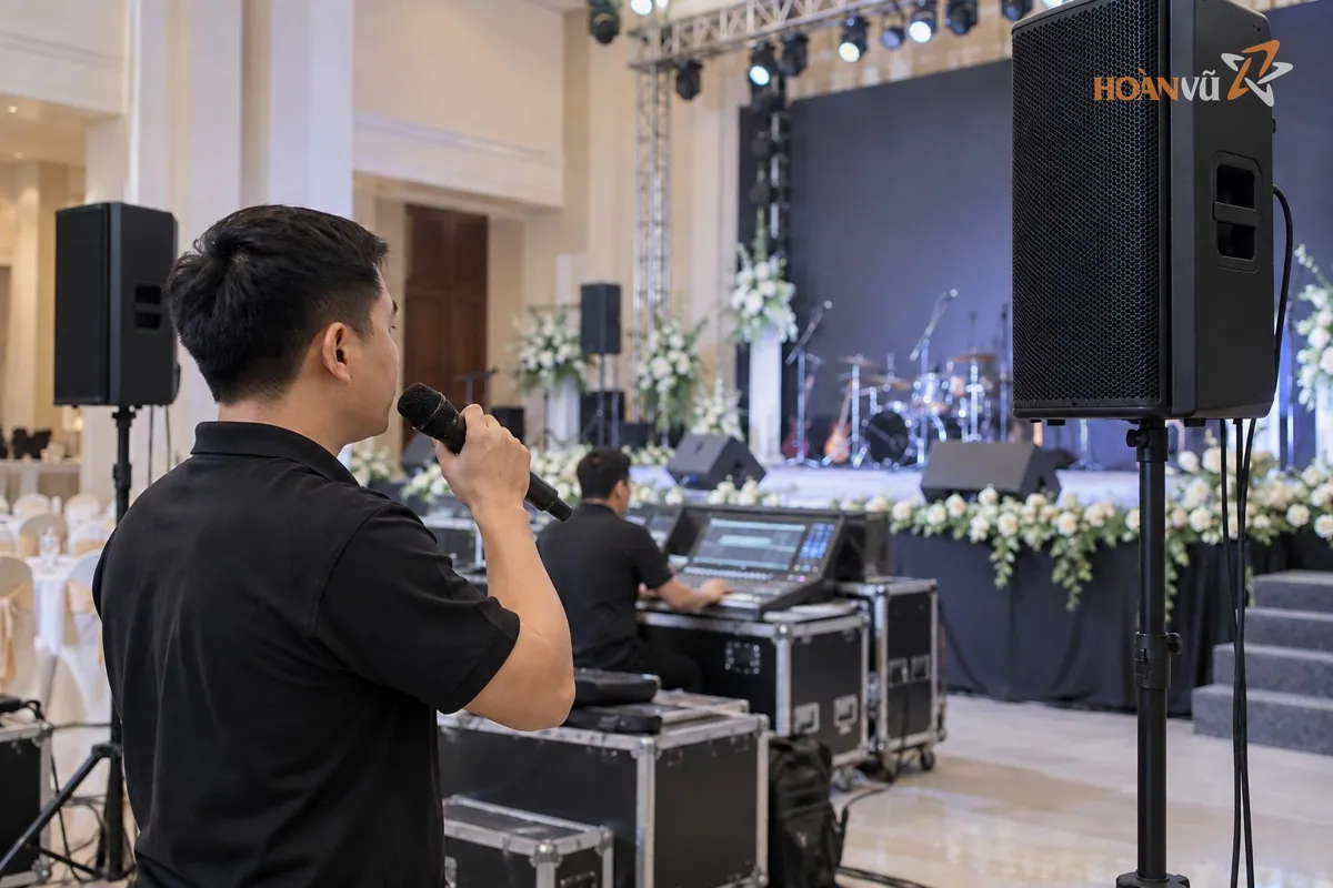 Kỹ thuật viên cầm micro không dây kiểm tra âm thanh, loa đặt trên chân trước sân khấu