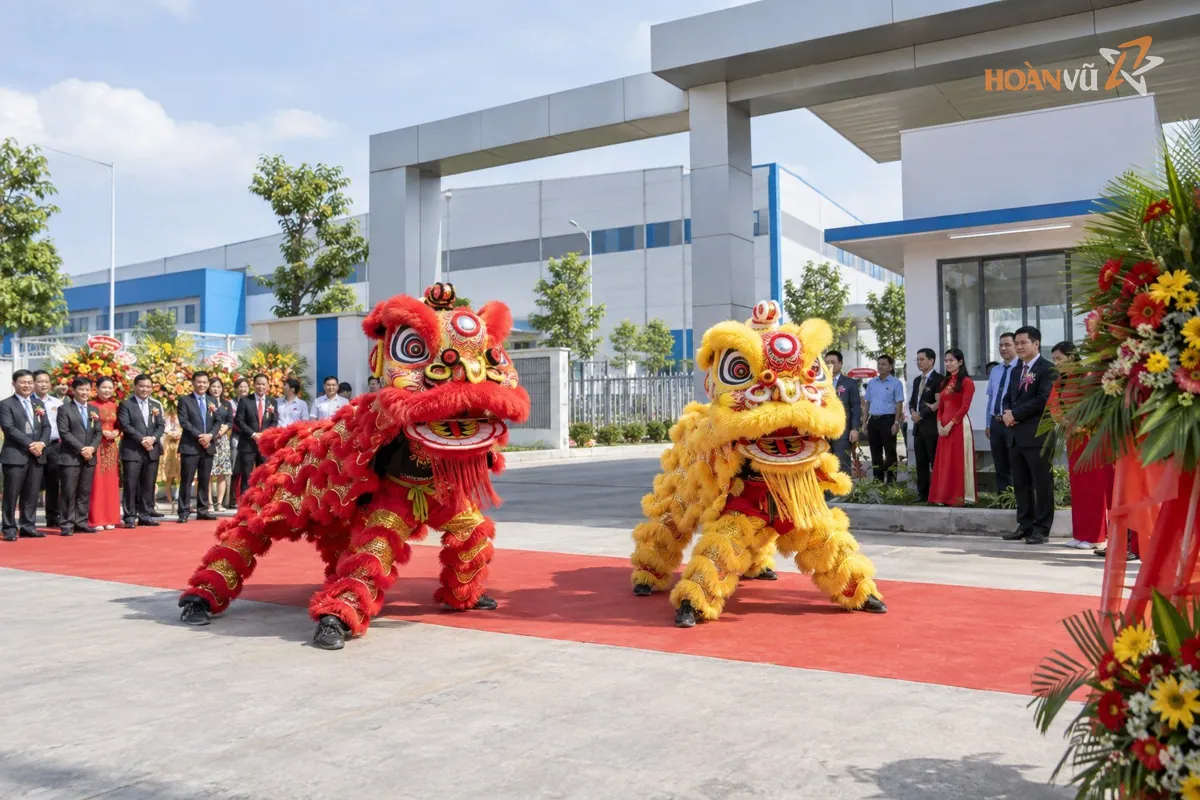 Đoàn múa lân vàng đỏ biểu diễn trước cổng nhà máy trong lễ khánh thành, khách mời đứng xem