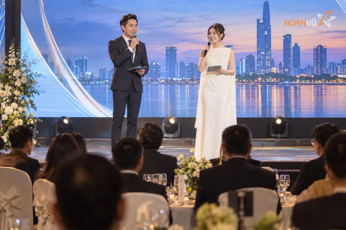 MC nam và MC nữ cầm micro dẫn chương trình trên sân khấu hội nghị doanh nghiệp, màn hình